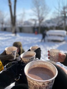 two people holding cups of hot chocolate in the snow with their hands on each other