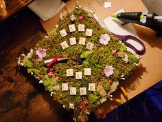 a moss covered box with letters and flowers on the top, surrounded by scissors and other crafting supplies