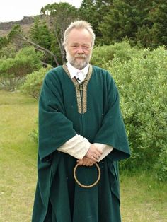 an older man dressed in green and white with a ring around his neck, standing outside