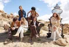 a group of people sitting on top of a chair in the dirt near some rocks