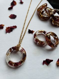 three necklaces and two rings on a table with rose petals scattered around the items