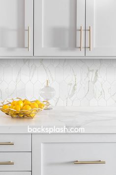 a bowl filled with lemons sitting on top of a counter next to white cabinets