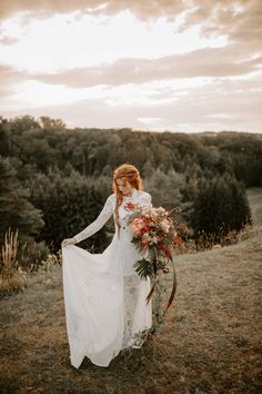 a woman standing on top of a lush green hillside holding a bouquet of flowers in her hand