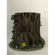 a tree stump with a house built into it's side and flowers around the base