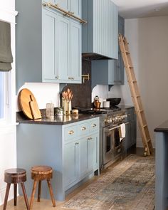 a kitchen with blue cabinets and wooden stools in it, along with a ladder leading up to the window