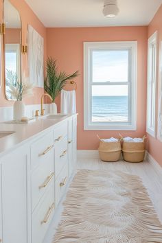 a bathroom with pink walls, white cabinets and beige rugs on the floor in front of two windows