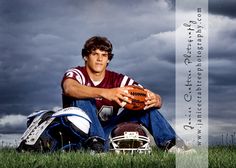 a man sitting in the grass with a football and helmet on his lap, under a cloudy sky