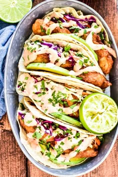 fish tacos in a bowl with lime wedges on the side