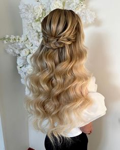 a woman with long blonde hair is standing in front of white flowers and has her back to the camera