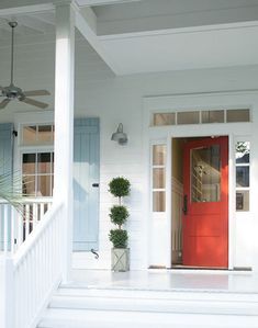 a red door on a white house with blue shutters and potted plants in front