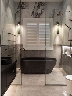 a bathroom with marble walls and flooring has a black bathtub in the middle