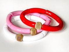 This colorful red and pink bracelet set of 3 is perfect for stacking and mixing and matching year round. The skinny acrylic tubes allow for multiple bracelets to be worn in a comfortable stack all day. Each set comes with a pink, red and white bracelet. Acrylic bracelets are 7 3/4 inches in diameter and fit most women (size medium). If you have a smaller wrist, these will slide a bit more like a bangle (tip: the more you stack, the less they slide). Each bracelet is made of 8mm acrylic tube beads and finished with a bone bead to complete the look. Stack, mix and match, and have fun with these beauties! Materials: - Acrylic - Bone Packaging: All jewelry is handmade in Chattanooga, TN and packaged in a white jewelry box with black and white gingham bow - ready to gift or unwrap yourself! --- Red Plastic Bracelet Jewelry, Trendy Red Plastic Bracelets, Trendy Red Plastic Bracelet, Red Plastic Beaded Bracelets As Gift, Adjustable Red Beaded Plastic Bracelets, Trendy Red Stackable Beaded Bracelets, Trendy Red Stackable Bracelets, Stacked Beaded Bracelets, Bracelets Pink