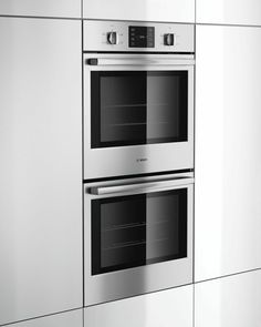 two silver ovens side by side in a white kitchen with stainless steel cabinets and drawers