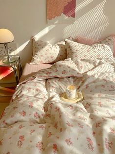 an unmade bed with pink and white flowers on the comforter next to a lamp