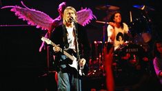 an image of a man that is on stage with his guitar and angel wings in the background