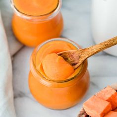 two jars filled with orange colored liquid next to sliced carrots and a wooden spoon