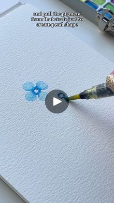 someone is using a paintbrush to draw blue flowers on white paper with watercolor pencils