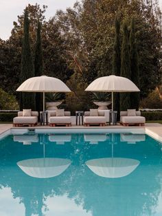 two lounge chairs with umbrellas next to a swimming pool