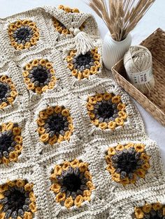 a crocheted blanket with sunflowers on it next to a basket and yarn