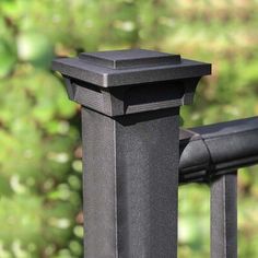 a close up of a black metal railing with green trees in the backgroud