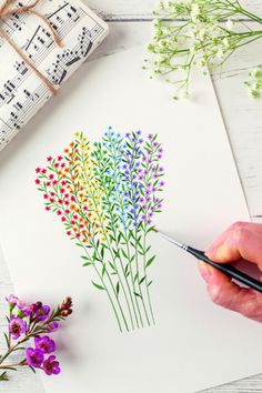 someone is painting flowers on paper with watercolors and music sheets in the background