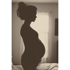 a pregnant woman standing on top of a bed next to a white curtain and window