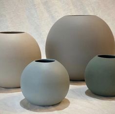 three white vases sitting next to each other on top of a cloth covered floor