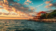 a house sitting on top of a rocky shore next to the ocean at sunset with clouds in the sky