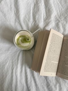 an open book sitting on top of a bed next to a cup of green liquid