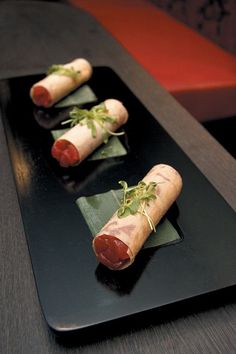 three hotdogs on a black plate with green garnish