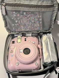 a pink camera sitting inside of a gray bag on top of a white table next to other items