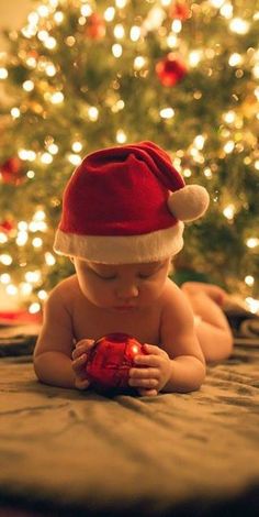 a baby wearing a santa hat on top of a bed next to a christmas tree