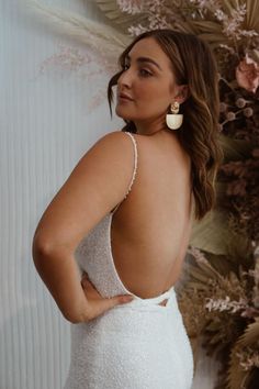 the back of a woman wearing a white wedding dress and gold earrings, standing in front of a floral wall