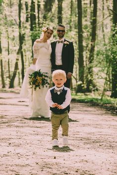 a little boy standing in the middle of a dirt road next to a bride and groom