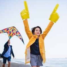 two people walking on the beach with their arms in the air and one holding a kite