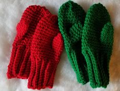 two red and green knitted mittens sitting next to each other on a white surface