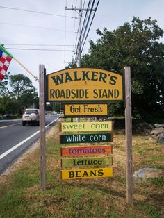 a wooden sign sitting on the side of a road next to a lush green field