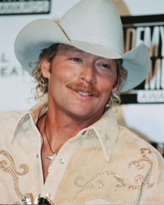 a man wearing a white cowboy hat smiling at the camera