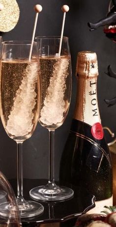 two champagne flutes filled with sparkling liquid and topped with toothpicks next to a bottle of wine