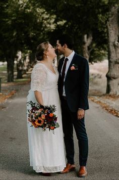 a bride and groom kissing on the street in front of some trees with orange flowers