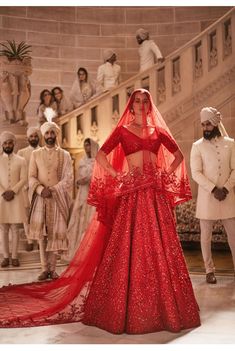 a woman in a red gown and veil stands on the stage with other people behind her