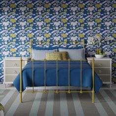 a bed with blue sheets and pillows in front of a floral wallpaper