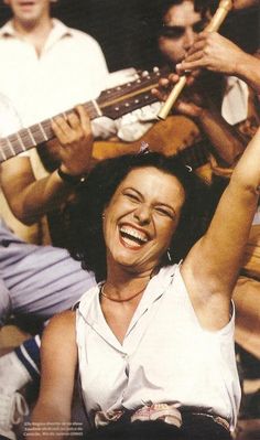 a woman is smiling and holding her guitar up in the air with other people behind her