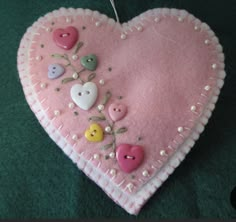 a pink heart with buttons and flowers on it sitting on a green carpeted floor