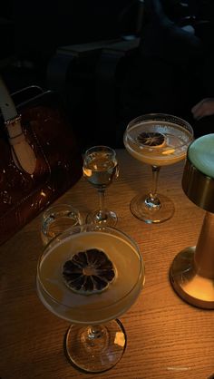 three wine glasses sitting on top of a wooden table next to a lamp and purse