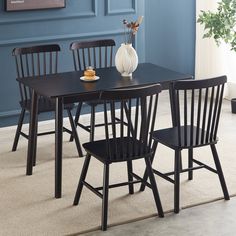 a dining room table with four chairs and a vase on top of it in front of a blue wall