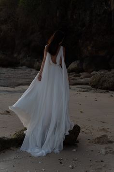 a woman standing on top of a sandy beach next to the ocean wearing a white dress