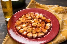 a red plate topped with cubed food next to a glass of beer and napkin