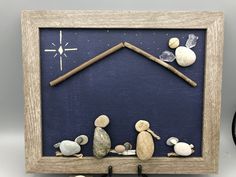 a nativity scene made out of rocks and wood is displayed in a frame on the wall