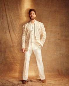 a man standing in front of a wall wearing a white suit